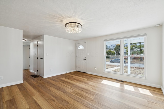 foyer featuring an inviting chandelier, a textured ceiling, and light wood-type flooring