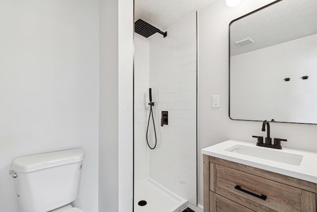 bathroom with vanity, a tile shower, a textured ceiling, and toilet