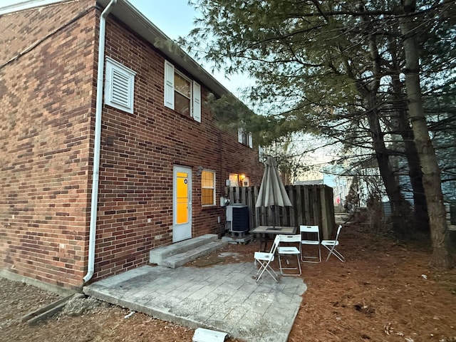 rear view of house with cooling unit, fence, brick siding, and a patio area