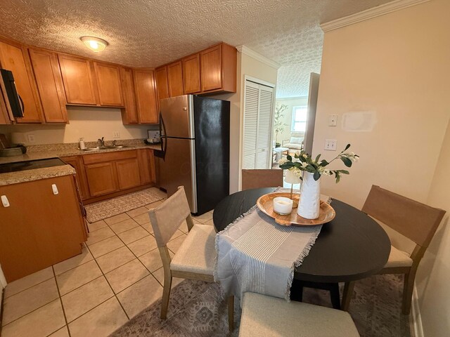 kitchen featuring a sink, freestanding refrigerator, crown molding, light countertops, and light tile patterned floors