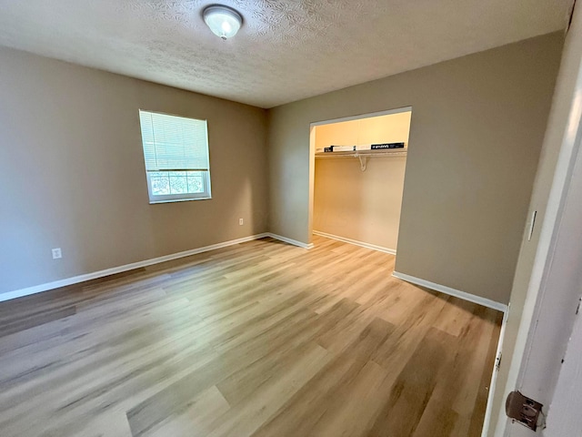 unfurnished bedroom with a closet, baseboards, a textured ceiling, and light wood finished floors