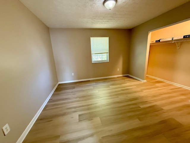 unfurnished bedroom with baseboards, light wood-type flooring, a closet, and a textured ceiling