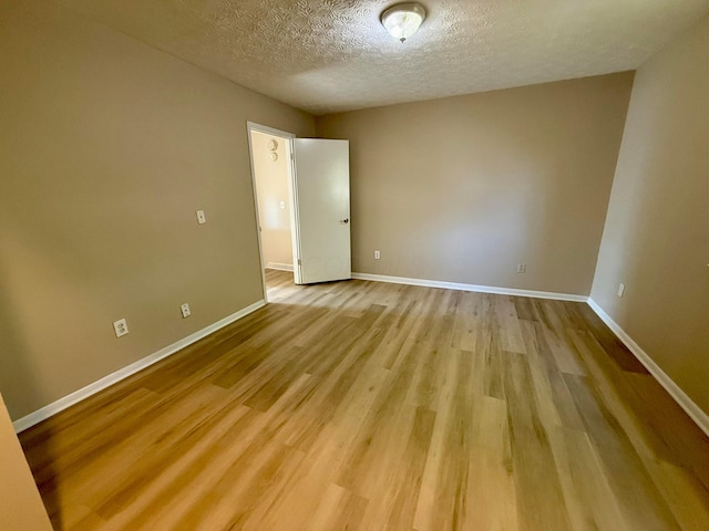 spare room with light wood-type flooring, baseboards, and a textured ceiling