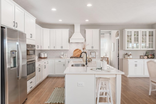 kitchen featuring custom exhaust hood, stainless steel appliances, an island with sink, and white cabinets