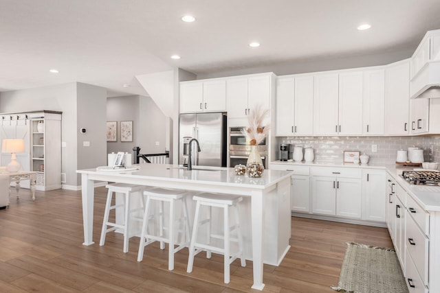 kitchen with appliances with stainless steel finishes, tasteful backsplash, white cabinetry, an island with sink, and light hardwood / wood-style flooring