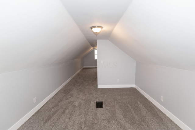 bonus room with dark carpet and vaulted ceiling