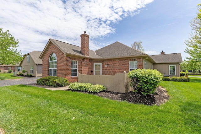back of property featuring a chimney, roof with shingles, brick siding, fence, and a yard