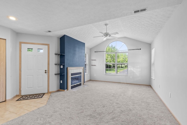 unfurnished living room featuring visible vents, ceiling fan, a tiled fireplace, and vaulted ceiling