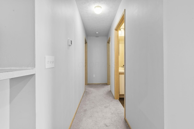 corridor featuring carpet floors, baseboards, and a textured ceiling