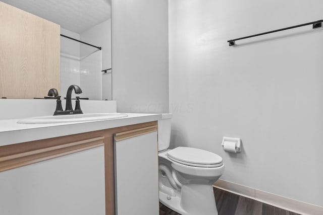 bathroom featuring vanity, wood finished floors, toilet, baseboards, and walk in shower