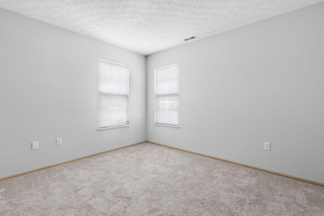 carpeted empty room featuring a textured ceiling, baseboards, and visible vents