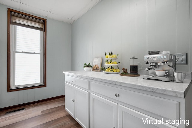 bar with plenty of natural light, light stone countertops, light hardwood / wood-style floors, and white cabinets