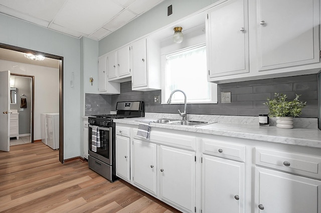 kitchen with white cabinets, washing machine and dryer, sink, and stainless steel gas range