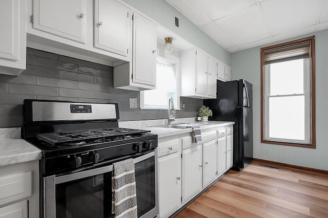 kitchen featuring stainless steel gas stove, white cabinetry, sink, light hardwood / wood-style floors, and black fridge