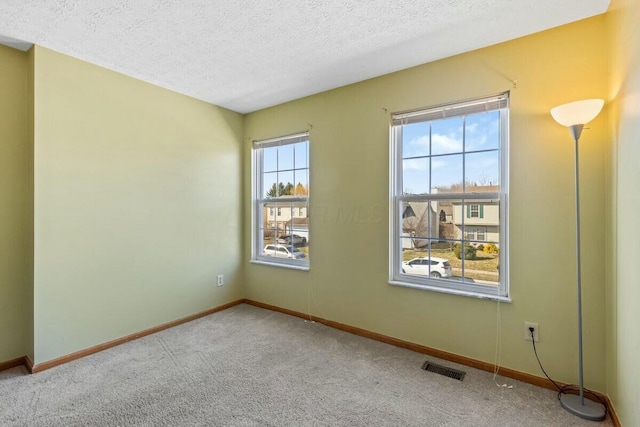 carpeted spare room with visible vents, a textured ceiling, and baseboards