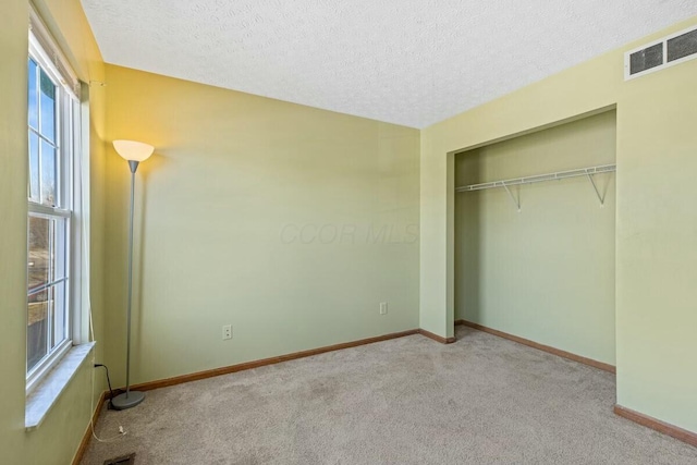 unfurnished bedroom with a textured ceiling, carpet floors, visible vents, baseboards, and a closet