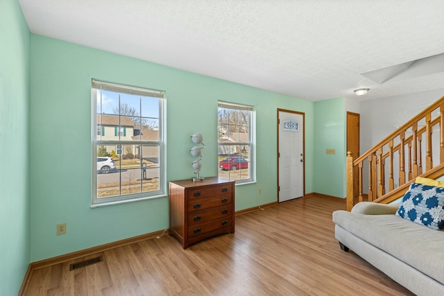 living room with light wood finished floors, visible vents, a textured ceiling, baseboards, and stairs