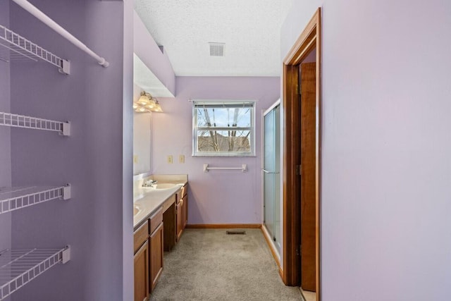 full bath with double vanity, visible vents, a stall shower, a sink, and a textured ceiling