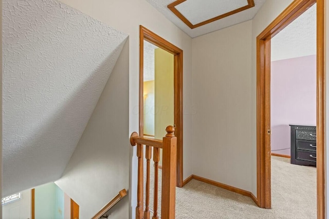 hallway with carpet floors, baseboards, and an upstairs landing