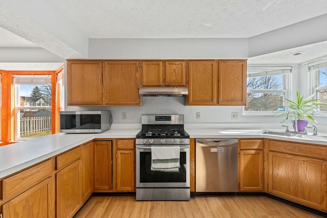 kitchen featuring stainless steel appliances, light countertops, a sink, and under cabinet range hood