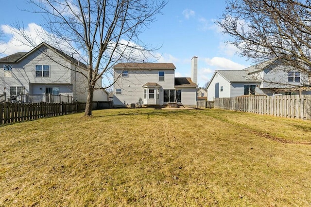 back of property featuring a yard, a chimney, and a fenced backyard