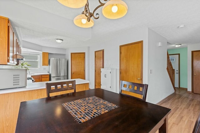 dining space with light wood-style floors, baseboards, stairway, and a textured ceiling