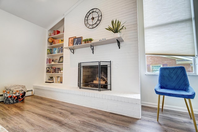 living room with built in shelves, vaulted ceiling, a brick fireplace, hardwood / wood-style floors, and a baseboard heating unit