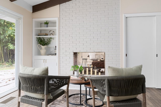 living area featuring brick wall, hardwood / wood-style floors, built in features, a fireplace, and beam ceiling