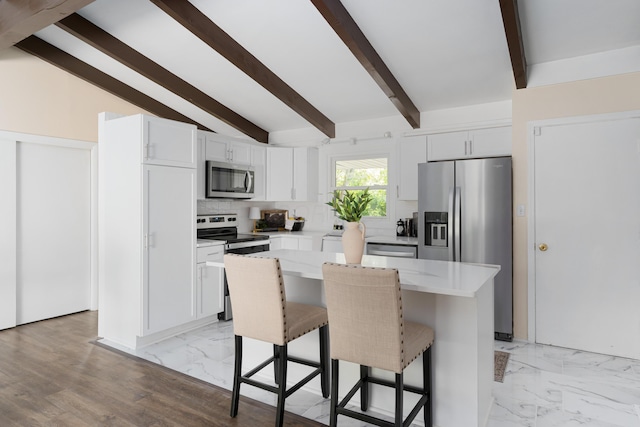 kitchen with a kitchen island, appliances with stainless steel finishes, a breakfast bar, white cabinetry, and decorative backsplash