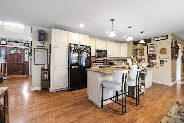 kitchen with a kitchen breakfast bar, hanging light fixtures, light stone counters, black appliances, and light wood-type flooring