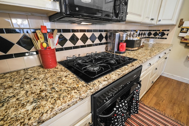 kitchen with light stone counters, wood-type flooring, black appliances, decorative backsplash, and white cabinets