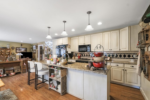 kitchen featuring a kitchen island with sink, light stone countertops, pendant lighting, and black appliances