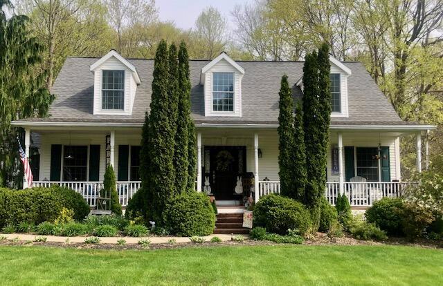 cape cod-style house featuring covered porch and a front yard