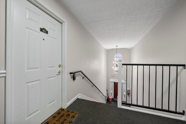 entrance foyer featuring baseboards, a textured ceiling, an inviting chandelier, and dark colored carpet