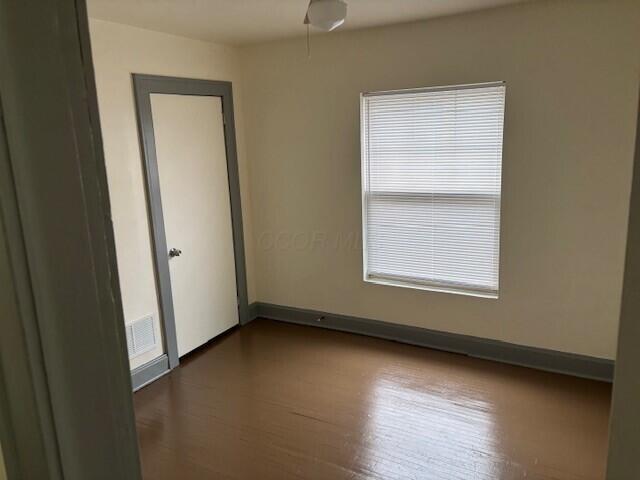 empty room with dark wood-style floors, baseboards, and visible vents