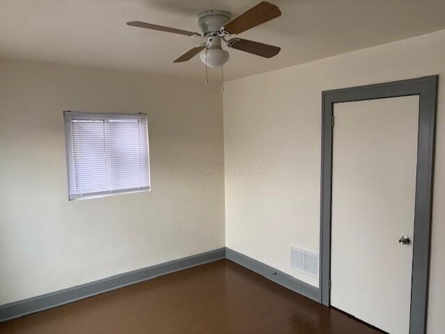 spare room featuring dark wood-type flooring, visible vents, ceiling fan, and baseboards