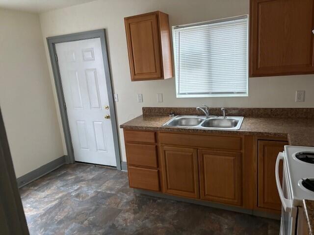 kitchen featuring brown cabinets, a sink, white electric stove, and baseboards