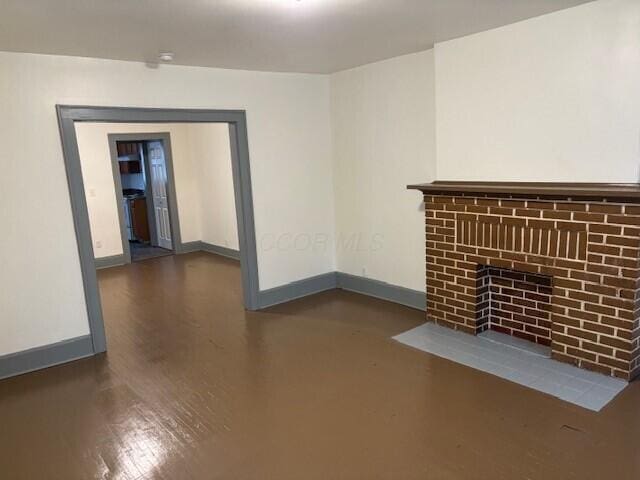 unfurnished living room with a fireplace, baseboards, and wood finished floors