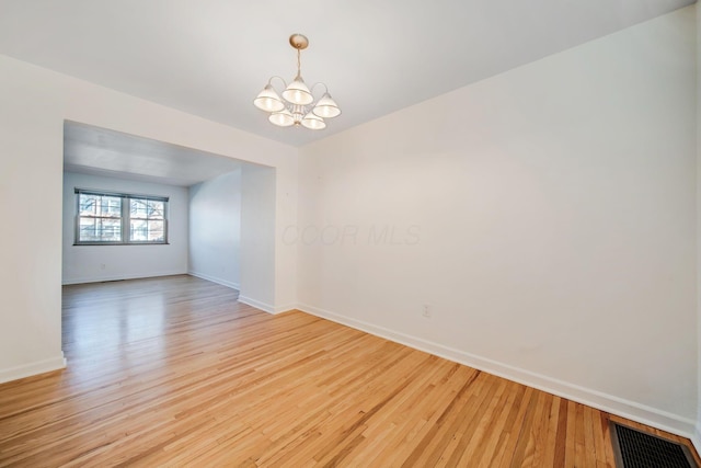 empty room featuring a notable chandelier and light hardwood / wood-style flooring