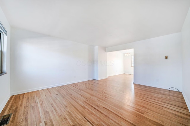 empty room featuring a notable chandelier and light wood-type flooring