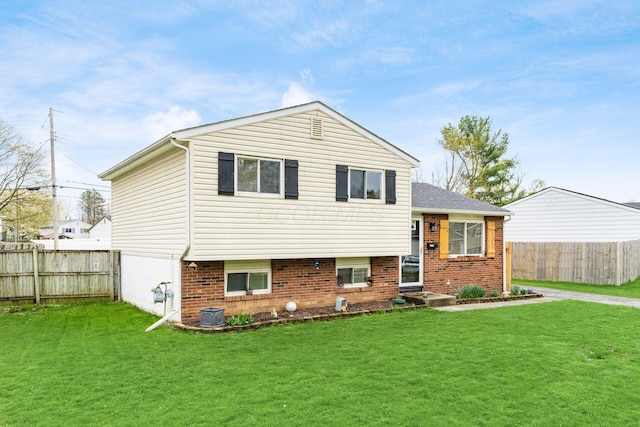 tri-level home featuring fence, a front yard, and brick siding