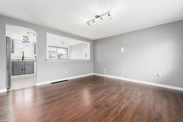 unfurnished living room with baseboards, visible vents, dark wood finished floors, and a sink