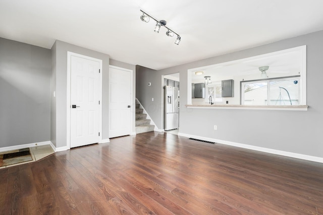 unfurnished living room with rail lighting, visible vents, stairs, and baseboards