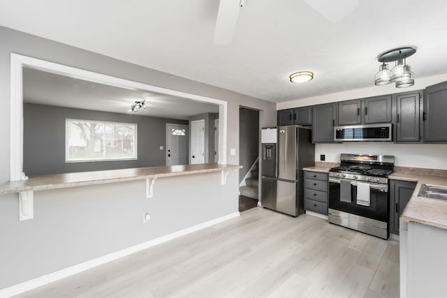 kitchen featuring light wood-style flooring, stainless steel appliances, light countertops, a kitchen bar, and baseboards