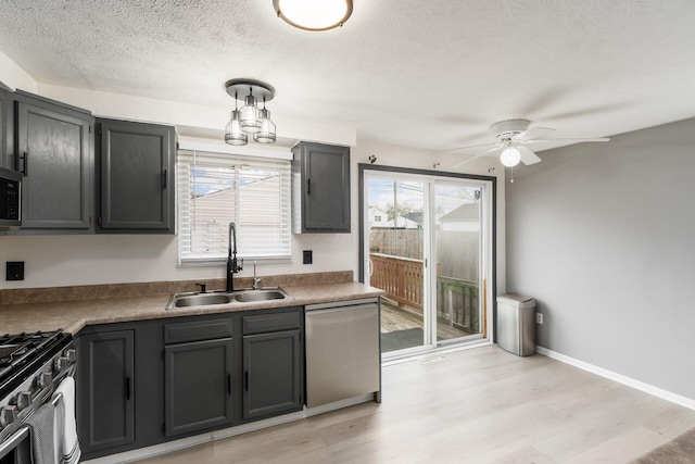 kitchen with light wood-style flooring, stainless steel appliances, ceiling fan with notable chandelier, a sink, and a textured ceiling