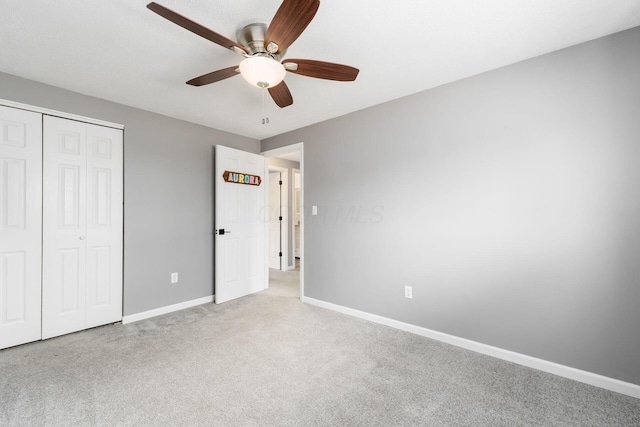 unfurnished bedroom featuring ceiling fan, a closet, baseboards, and light carpet