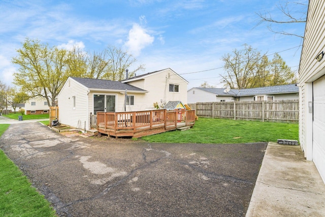 back of house with fence, roof with shingles, a deck, and a yard