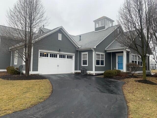 view of front of house with aphalt driveway, a front yard, an attached garage, and central AC unit