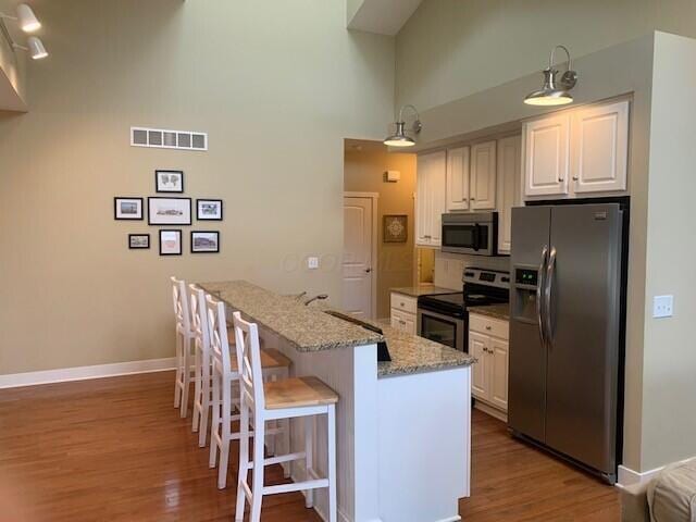 kitchen with light stone counters, dark wood-style floors, a breakfast bar area, appliances with stainless steel finishes, and white cabinets