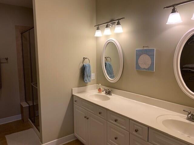 bathroom featuring double vanity, a stall shower, baseboards, and a sink